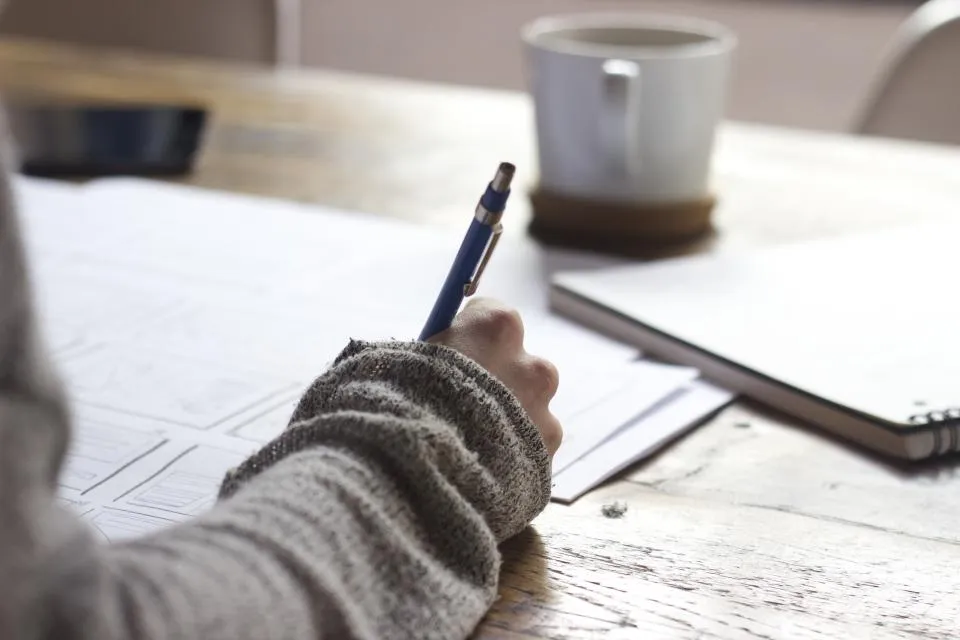 A hand writing notes beside a cup of coffee